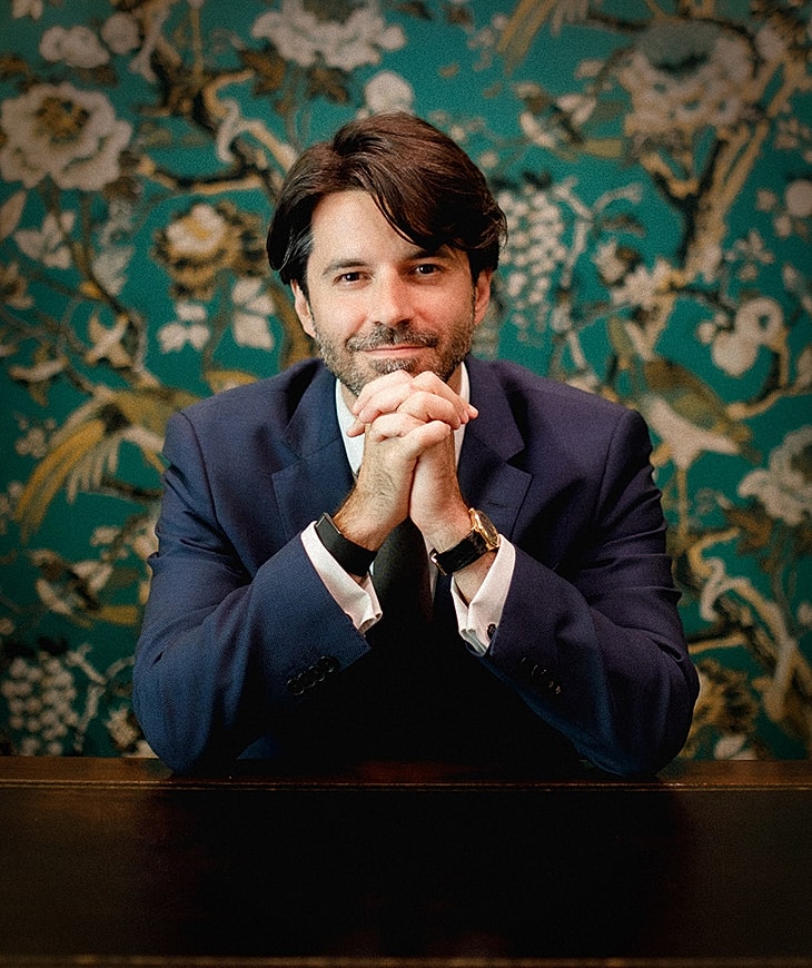 Man in suit with hands clasped thoughtfully.