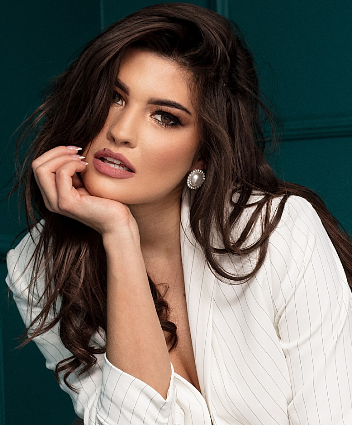 Woman with long hair posing thoughtfully in white blazer.