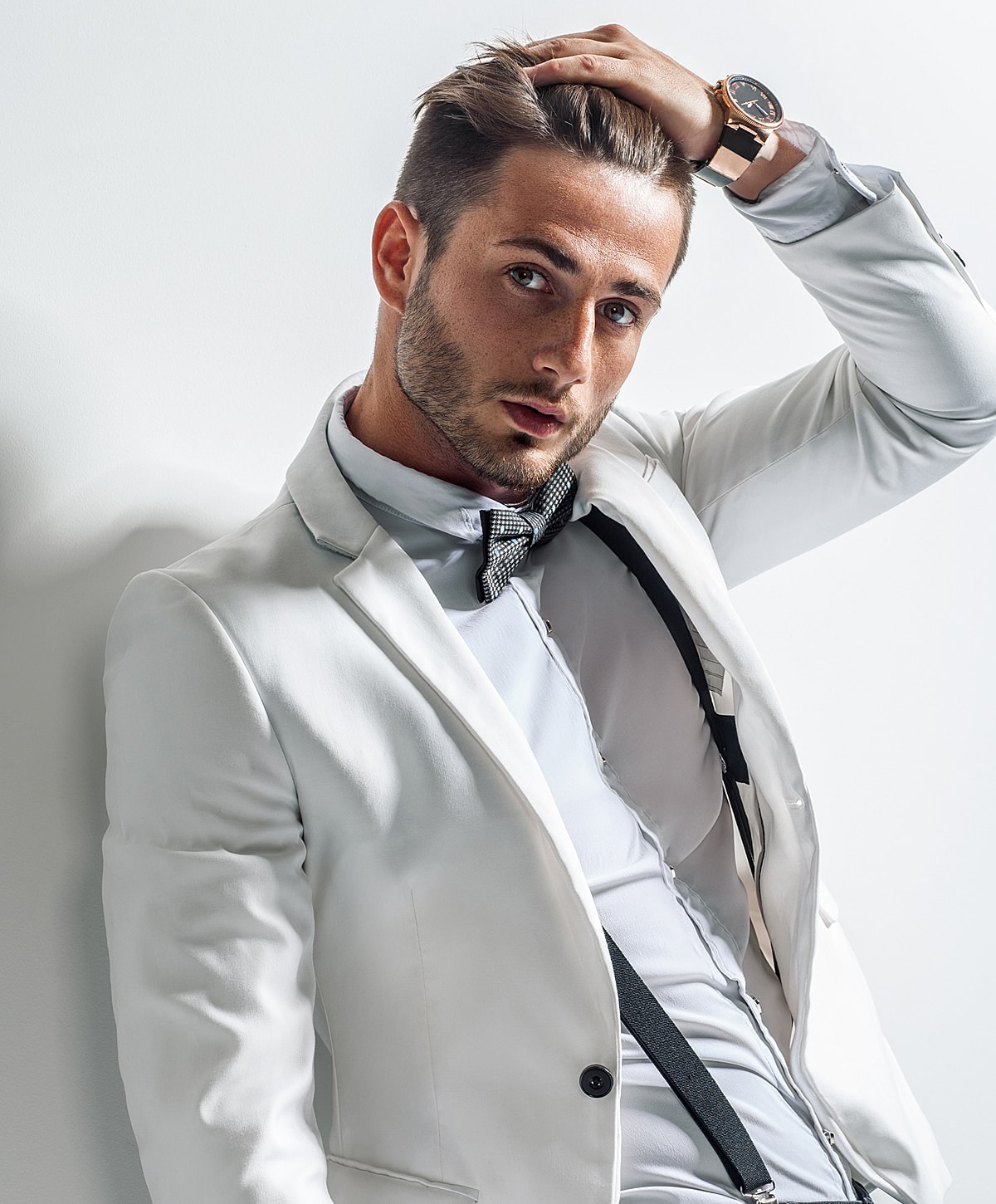 Man in white suit posing confidently against wall