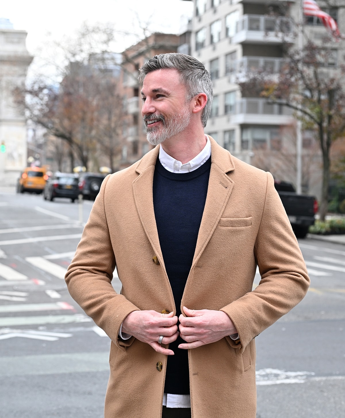 Man in stylish coat smiling on city street.