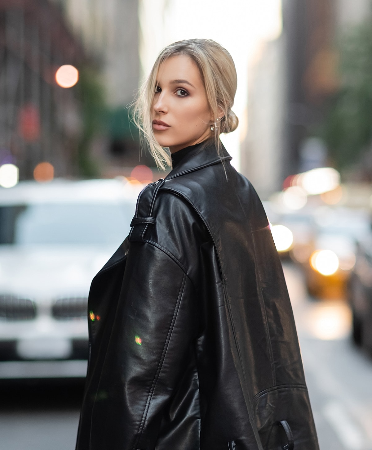 Woman in black leather jacket on city street.