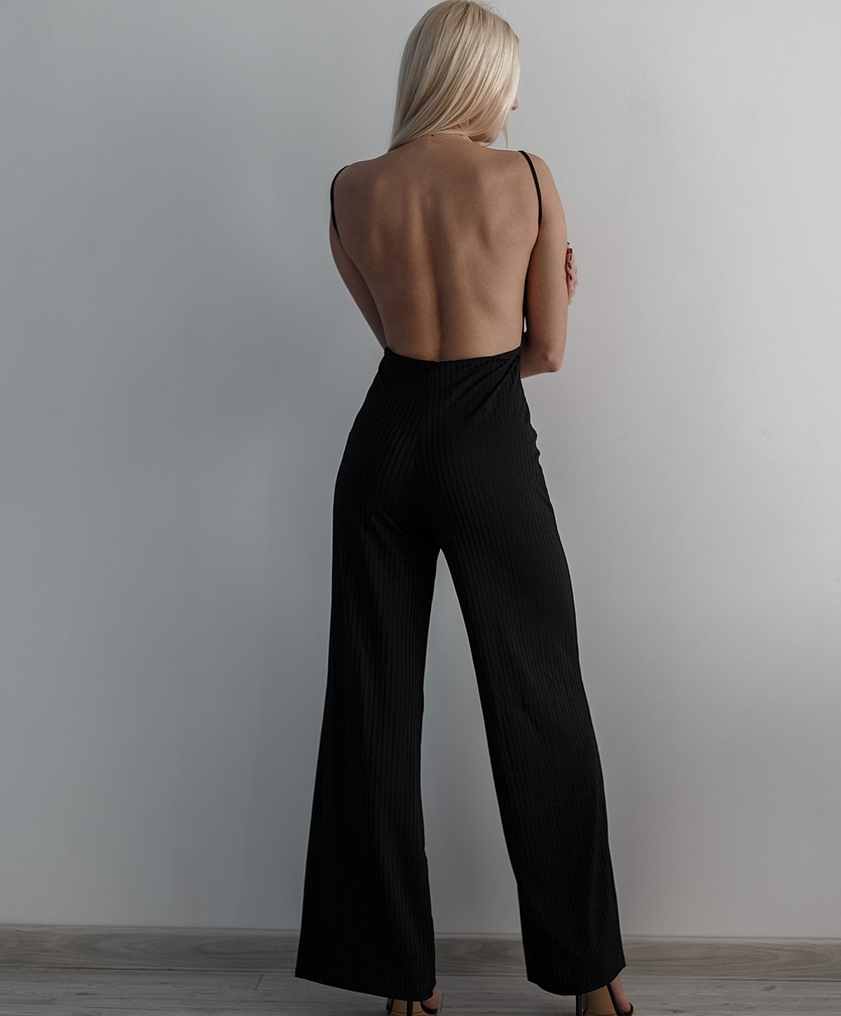 Woman in black backless jumpsuit, standing pose.