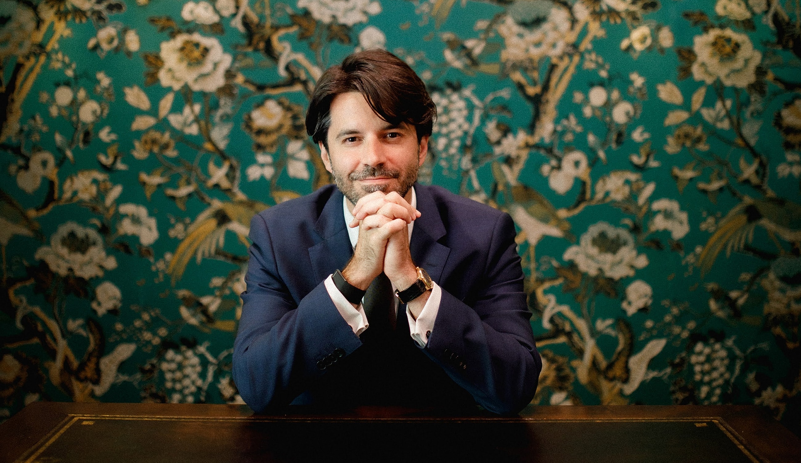 Man in suit against floral wallpaper background.